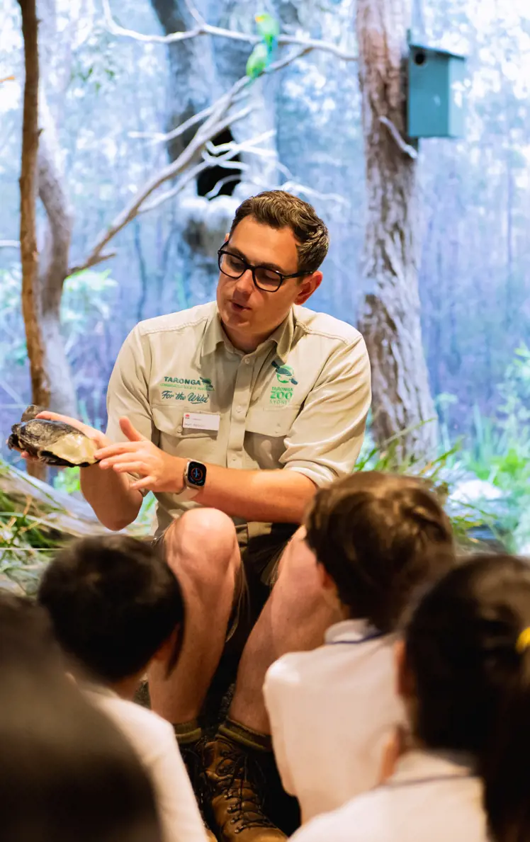 School students seated on the floor during a teacher‑led lesson in an immersive habitat classroom.