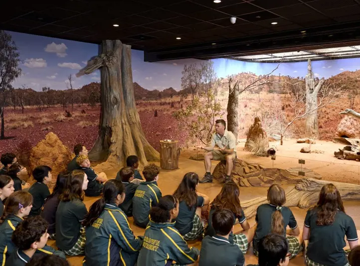 School students seated indoors listening to a guide in a desert-themed immersive classroom.