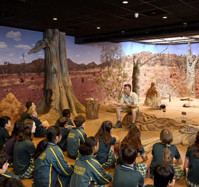 School students seated indoors listening to a guide in a desert-themed immersive classroom.