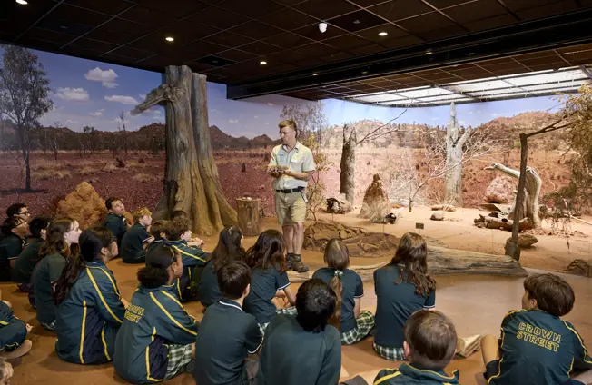 Students seated indoors listening to a guide in a desert-themed immersive classroom.