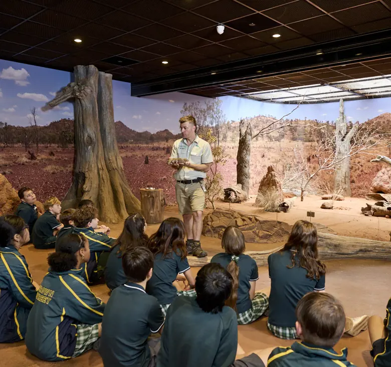 Students seated indoors listening to a guide in a desert-themed immersive classroom.