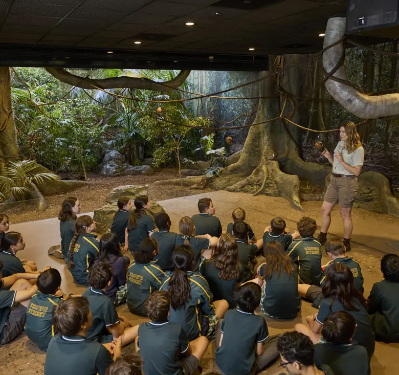 Students seated indoors listening to a teacher in a rainforest-themed immersive classroom.